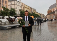The President of the Kraków Waterworks on Main Market in Krakow holds flowers and statue.