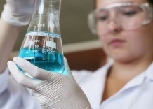 The laboratory technician holds a volumetric flask with a blue liquid in her hands.